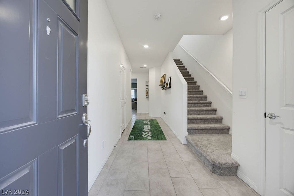 Crisp white walls and clean tile flooring define this welcoming entry hallway with adjacent stairs.