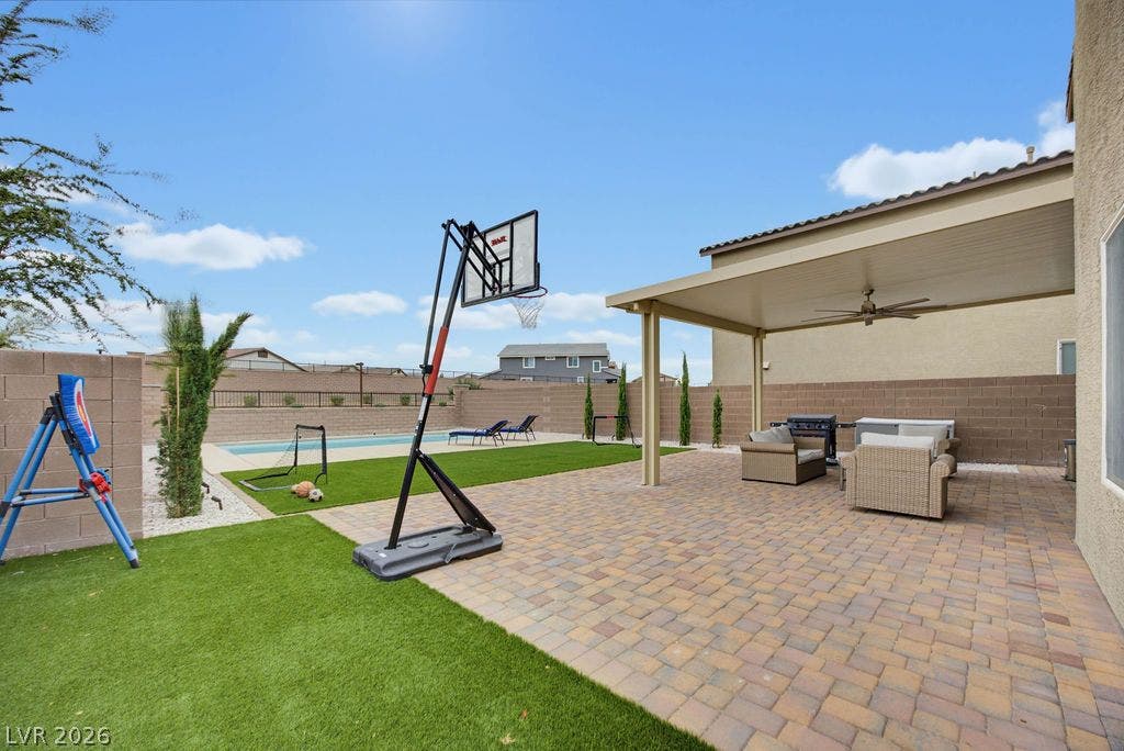 An inviting backyard patio paved with stone extends toward a sparkling in-ground pool.