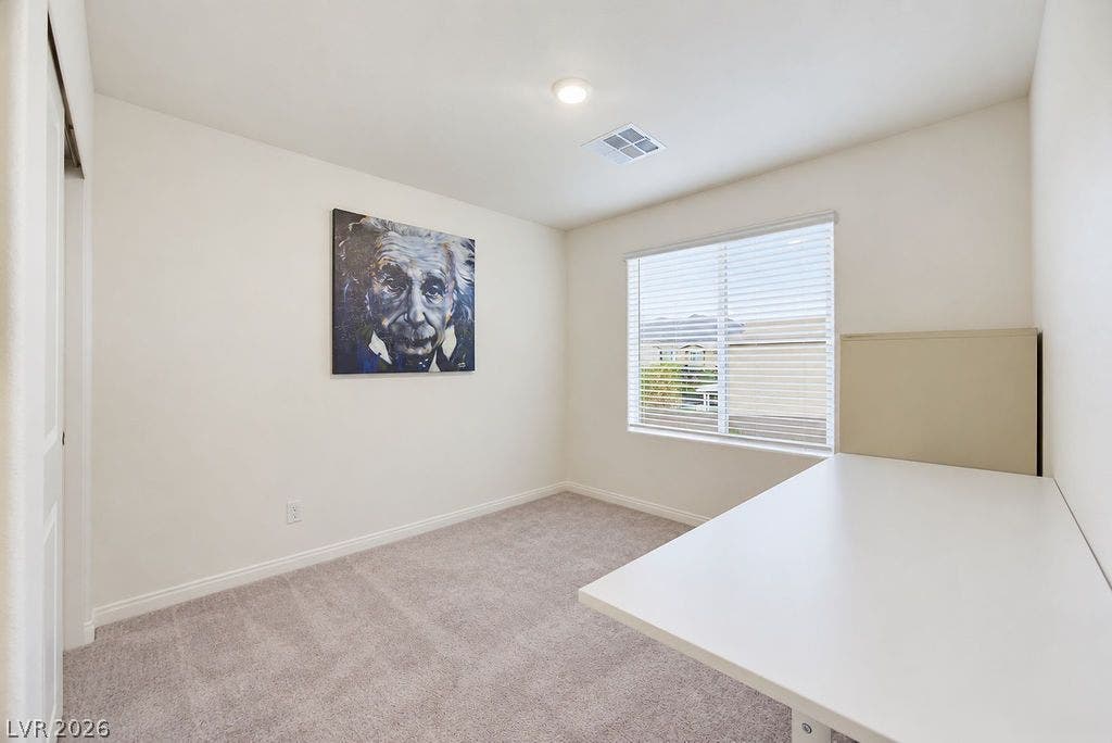 Plush carpeting and a large window create a comfortable, well-lit workspace or bedroom.