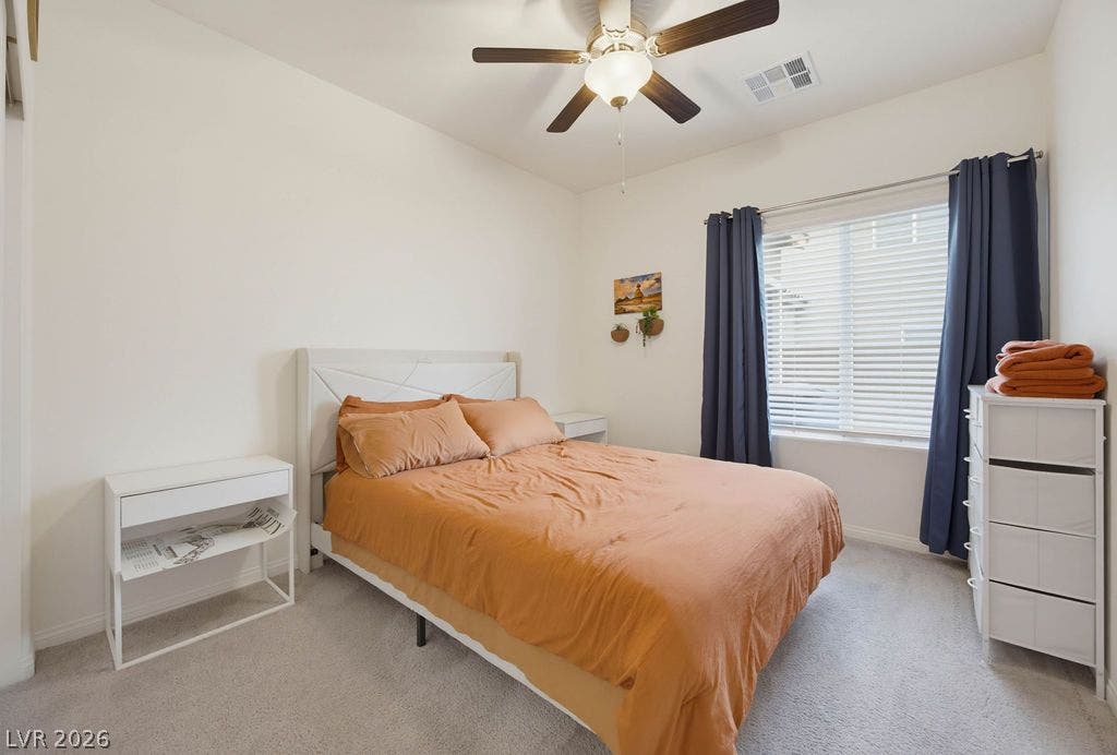 Plush carpeting and a large window create a serene atmosphere in this comfortable bedroom.