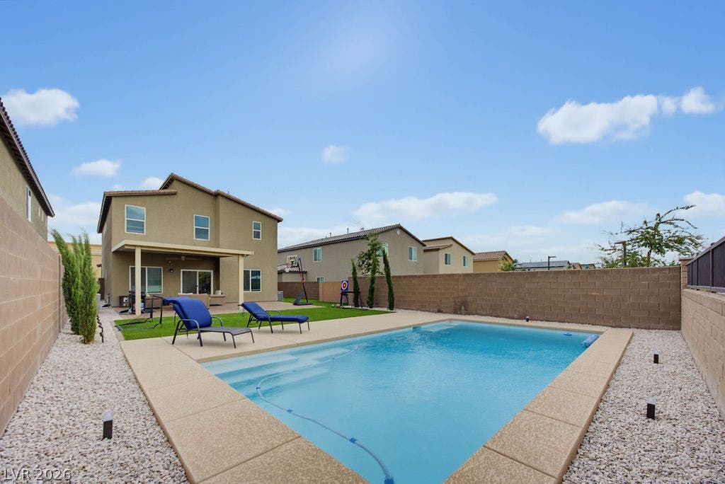An inviting backyard oasis features a sparkling swimming pool, manicured lawn, and a covered patio.