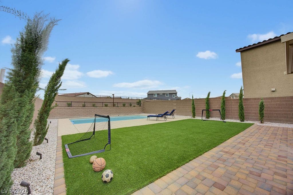 An inviting backyard features a sparkling in-ground pool bordered by manicured turf and brick pavers.