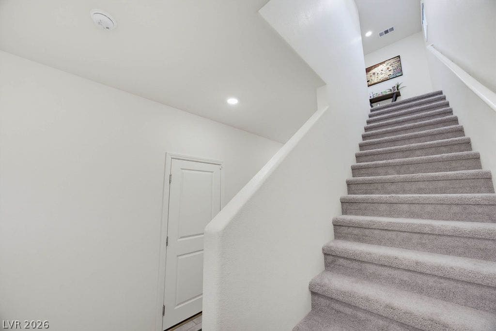 A carpeted staircase ascends past clean walls and recessed lighting.