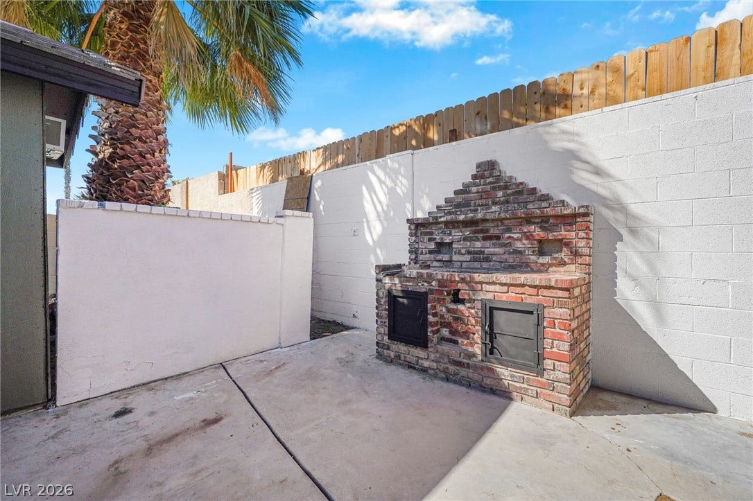 An outdoor brick fireplace stands ready for gatherings in the private concrete patio.