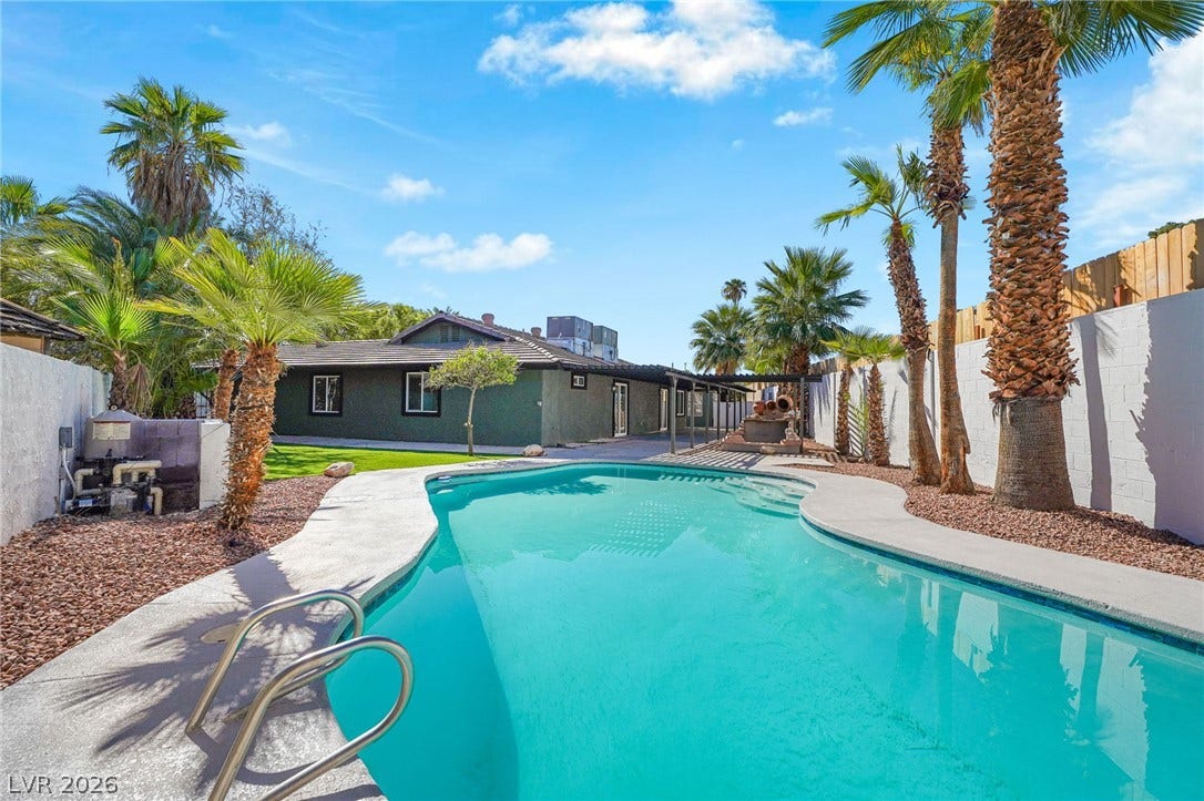 Palm trees frame a sparkling inground pool set against a manicured lawn and privacy fencing.
