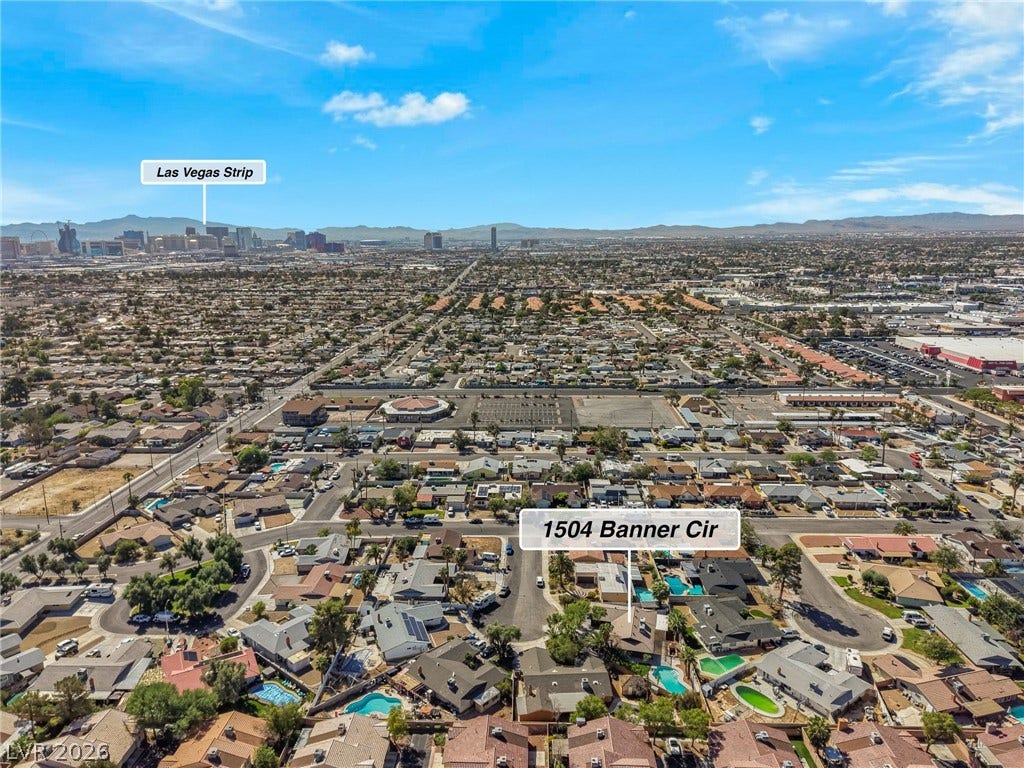 An aerial perspective showcases the surrounding neighborhood context and distant skyline views under clear skies.