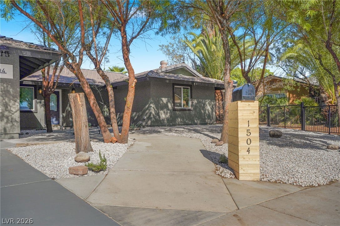 Mature trees shade the concrete walkway leading to this single-story home featuring stucco walls.
