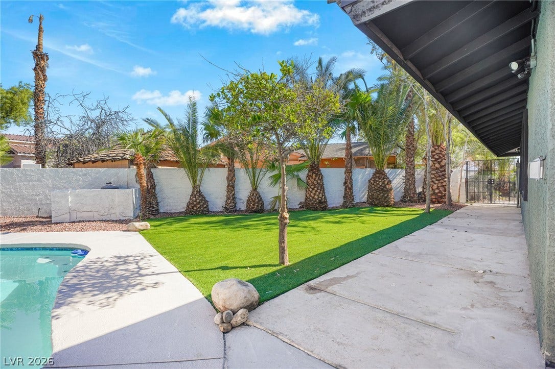 Lush palm trees line a secure walled backyard featuring a sparkling in-ground swimming pool.