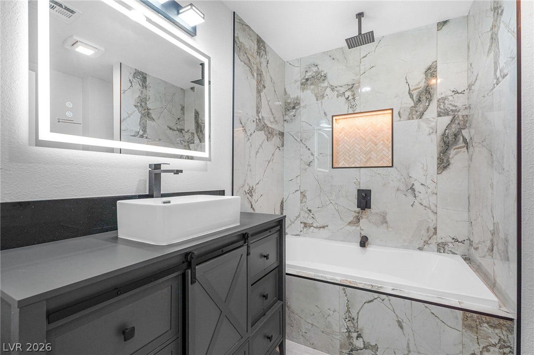 Floor-to-ceiling marble tile surrounds a sleek soaking tub in this updated bathroom.