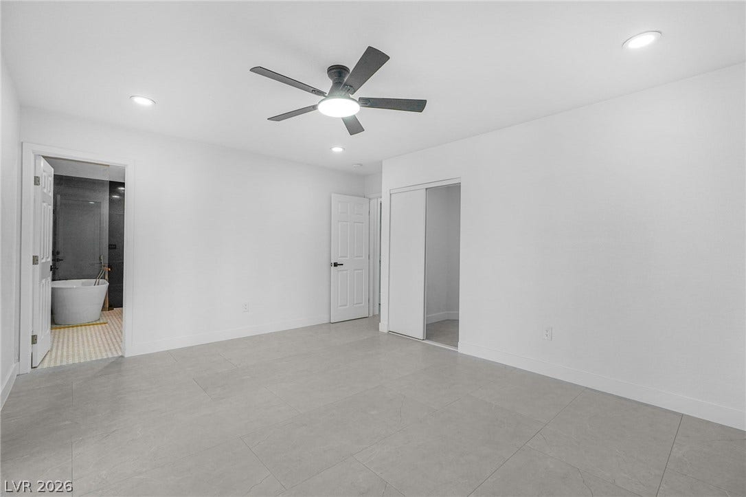 Clean lines and large format tile flooring define this modern primary suite with bathroom access.