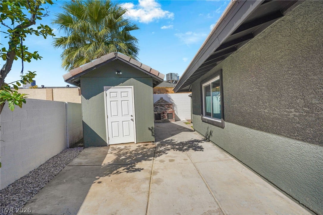 A spacious concrete side yard features stucco walls and a detached storage shed.