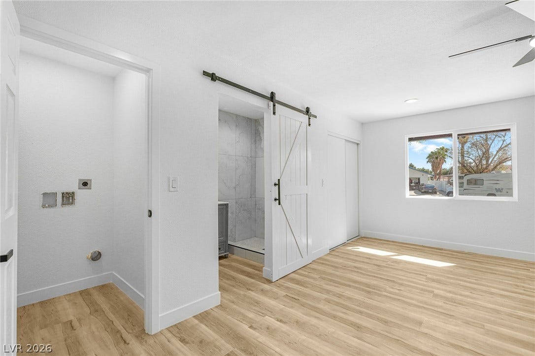 Smooth wood-look flooring and a sliding barn door create a modern, clean bedroom aesthetic.
