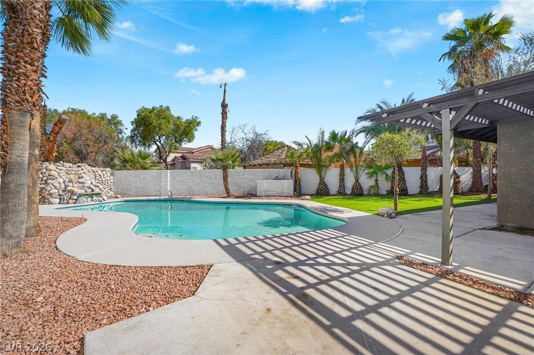 A sparkling in-ground pool is framed by mature palm trees and a shaded pergola structure.