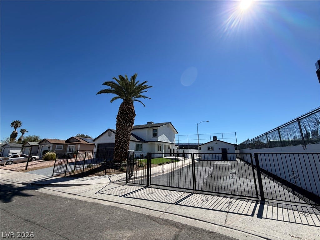 500 Grimsby Avenue, Henderson, NV 89014 Gated paved driveways lead toward a multi-level white stucco residence under clear sunny skies.