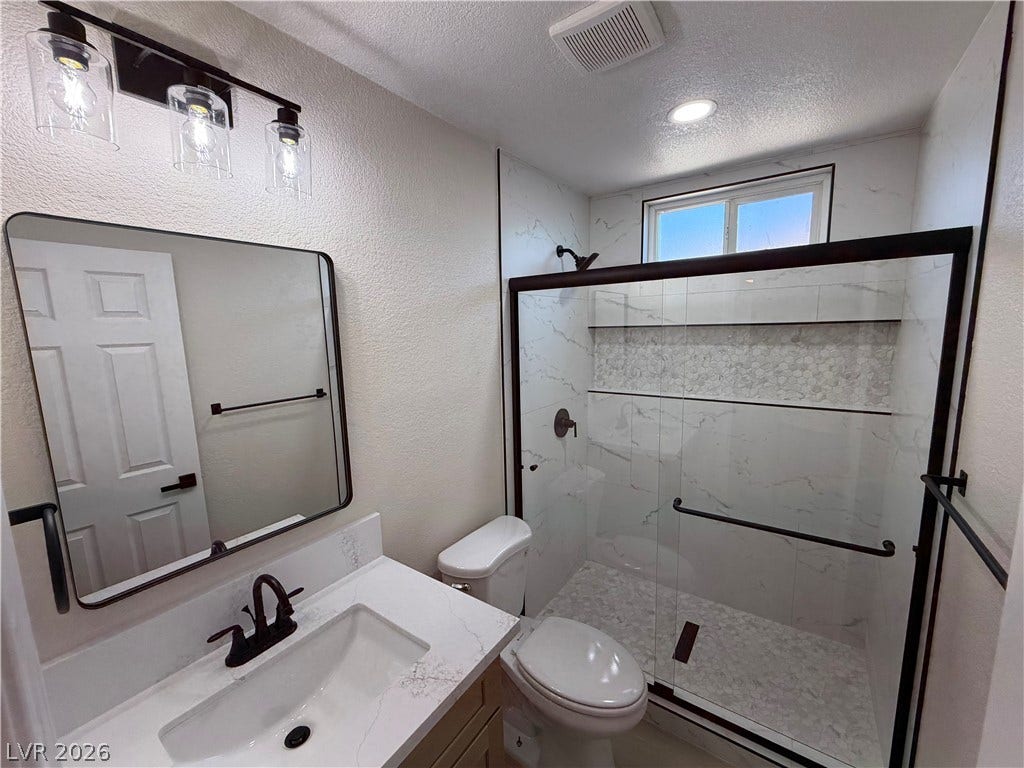 500 Grimsby Avenue, Henderson, NV 89014 A modern bathroom features a tiled walk-in shower alongside a stone-topped vanity.