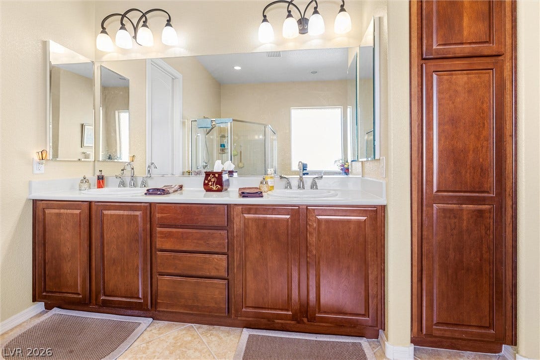 2107 Noah Tyler Ct., Henderson, NV 89052 A spacious double vanity anchors this bright bathroom featuring rich wood cabinetry and tile flooring.