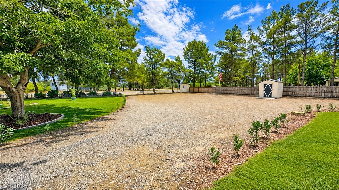 6130 Hawkins Way, Pahrump, NV 89061 Mature trees frame a spacious gravel driveway alongside lush green lawns and a practical storage shed.