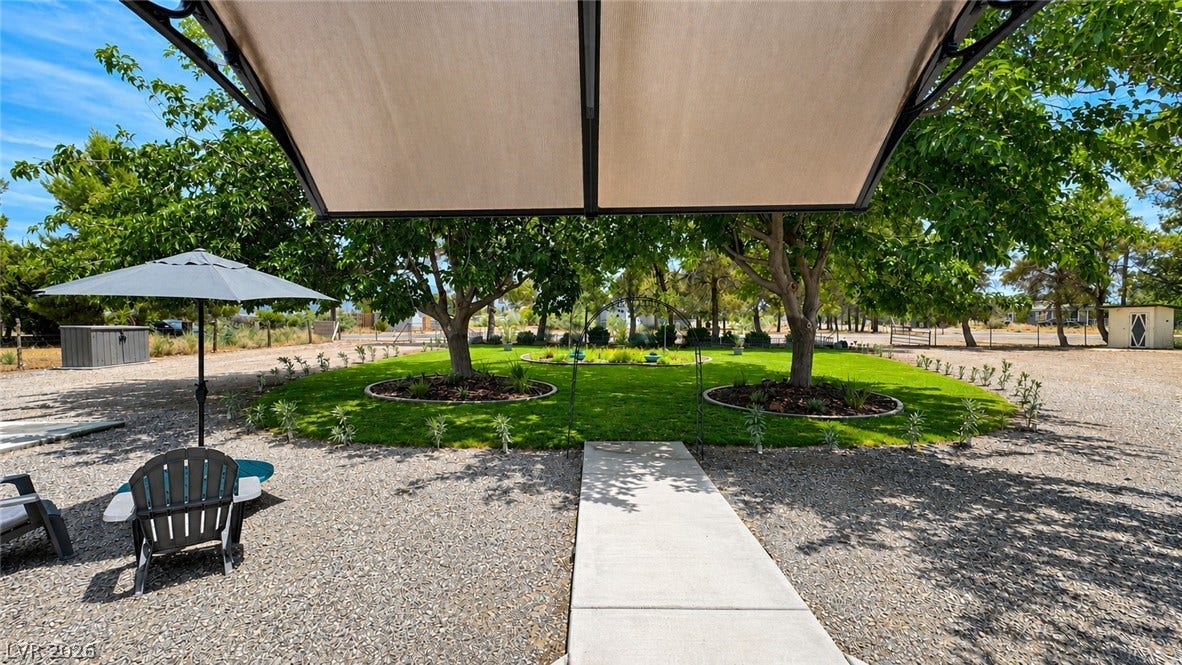 6130 Hawkins Way, Pahrump, NV 89061 A concrete walkway leads through a landscaped backyard with mature trees and a shaded patio.