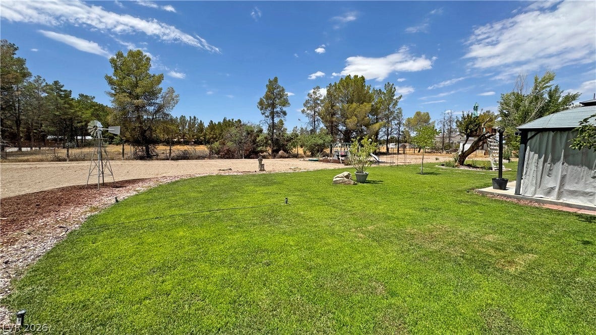 6130 Hawkins Way, Pahrump, NV 89061 Mature trees frame a spacious, grassy lawn underneath a wide open blue sky.