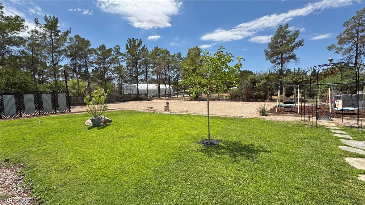 6130 Hawkins Way, Pahrump, NV 89061 Mature trees frame a spacious grassy lawn perfect for outdoor activities under sunny skies.