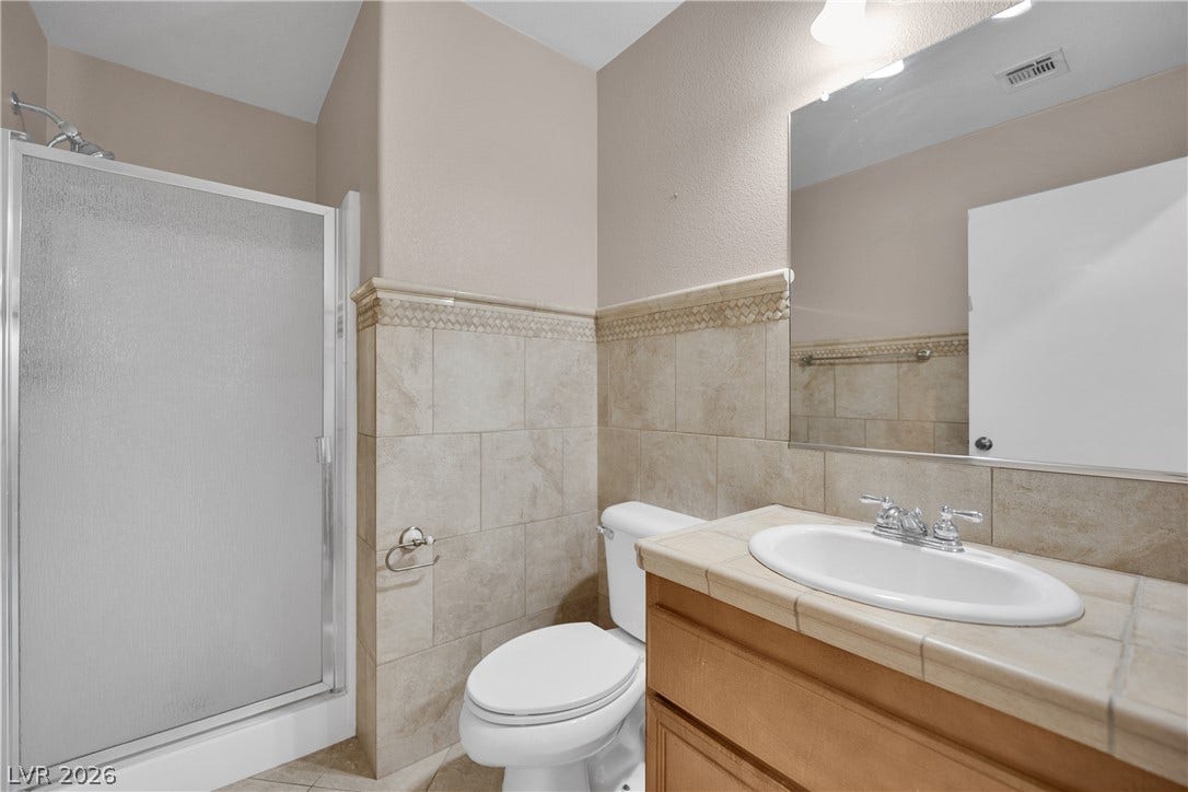 10149 Whitney Falls Court, Las Vegas, NV 89148 Tiled wainscoting and a matching tile-countertop vanity define this functional bathroom space.