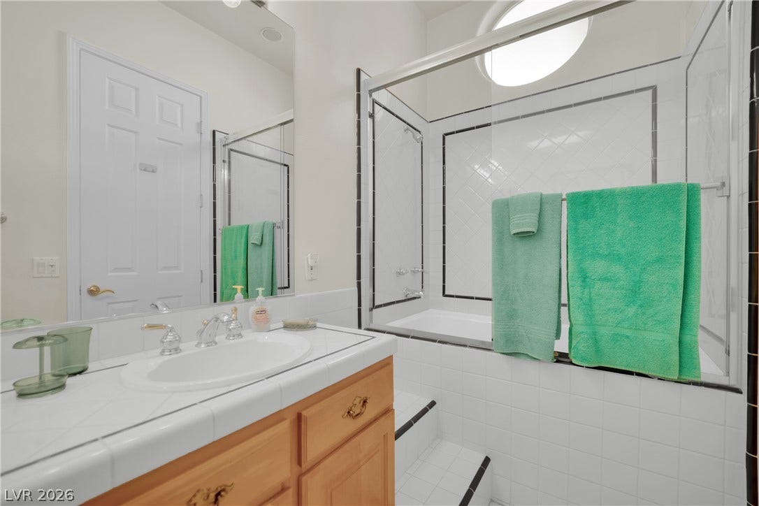 A glass-enclosed tub shower highlights this bright bathroom with a tiled vanity.