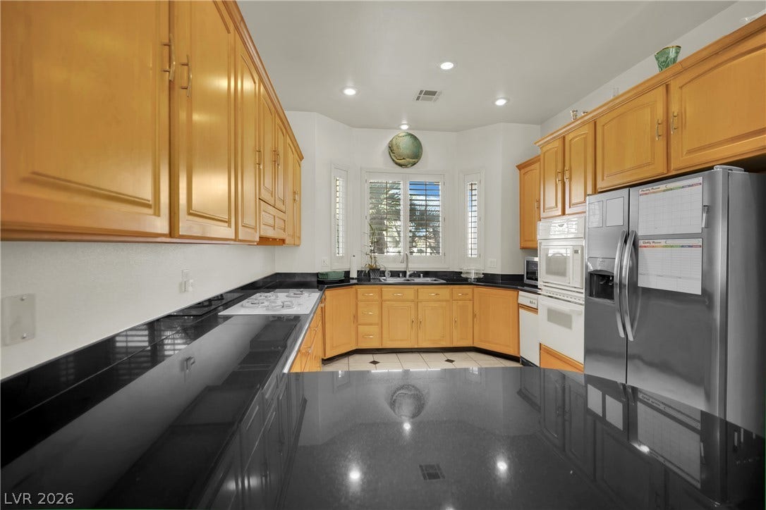 Polished granite countertops complement warm wood cabinetry and integrated appliances in this spacious kitchen.