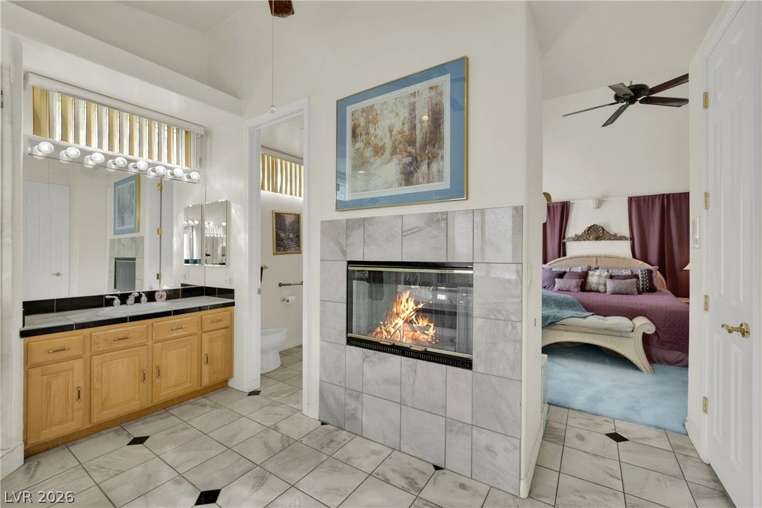 A dual-sided fireplace set in tile connects the private bath with the bedroom beyond.