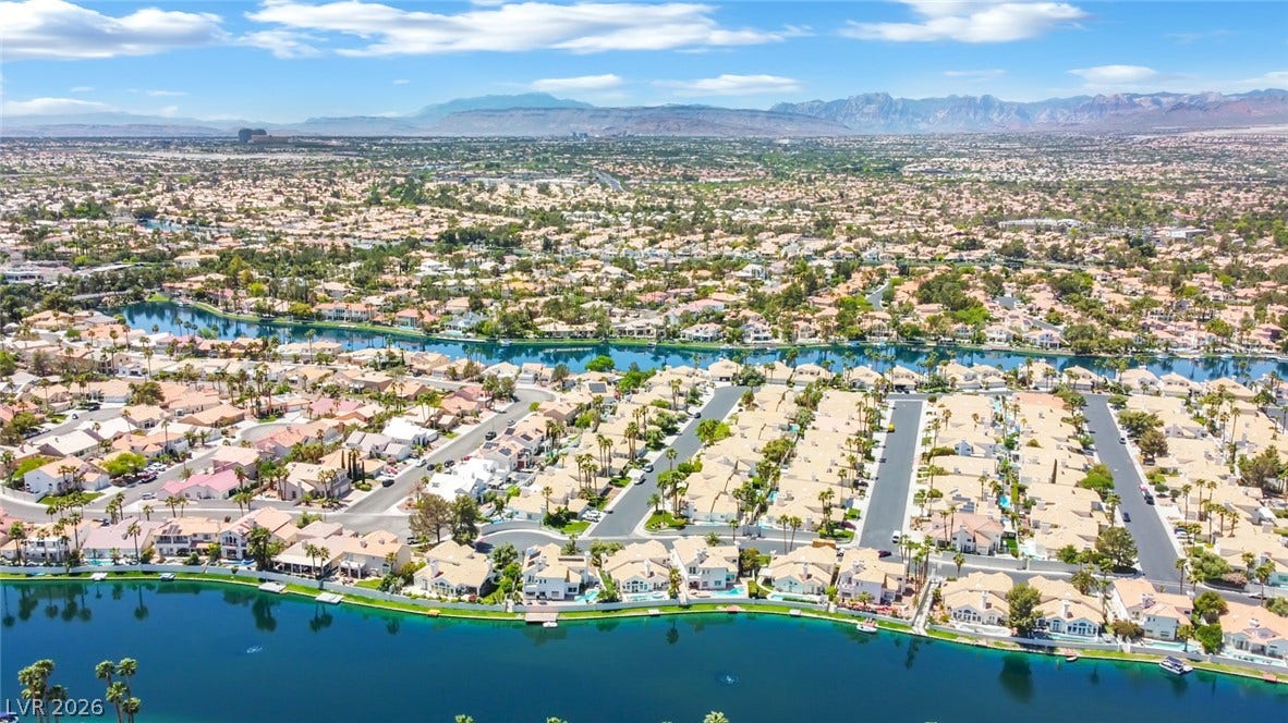 A sprawling neighborhood landscape is framed by winding waterways and majestic mountain peaks.