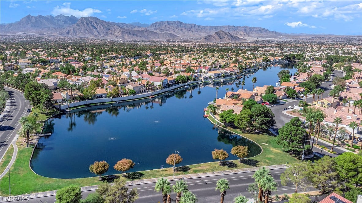 Dramatic mountain ranges frame a serene community lake surrounded by mature trees.
