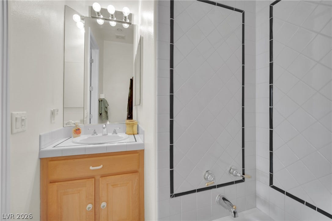 White tiled walls frame the tub and matching tile vanity top in this space.