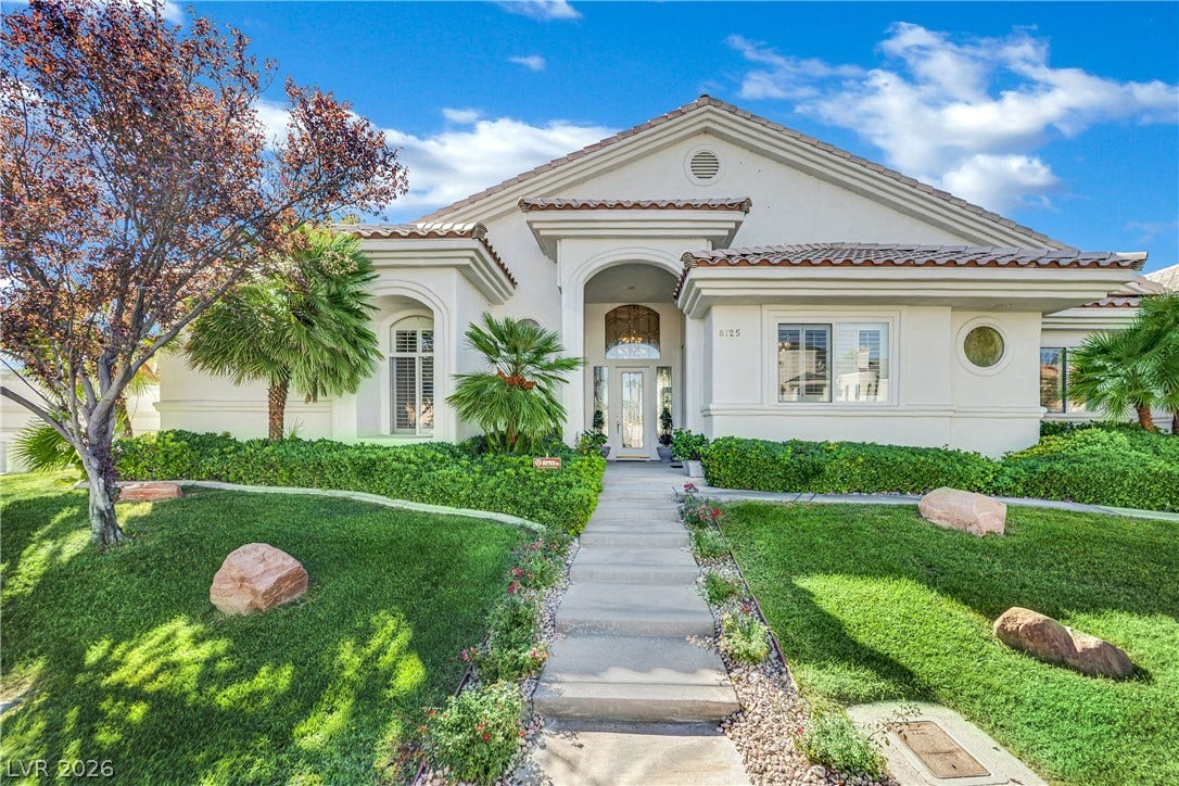 A concrete walkway leads past manicured lawns and palms to a covered main entrance.
