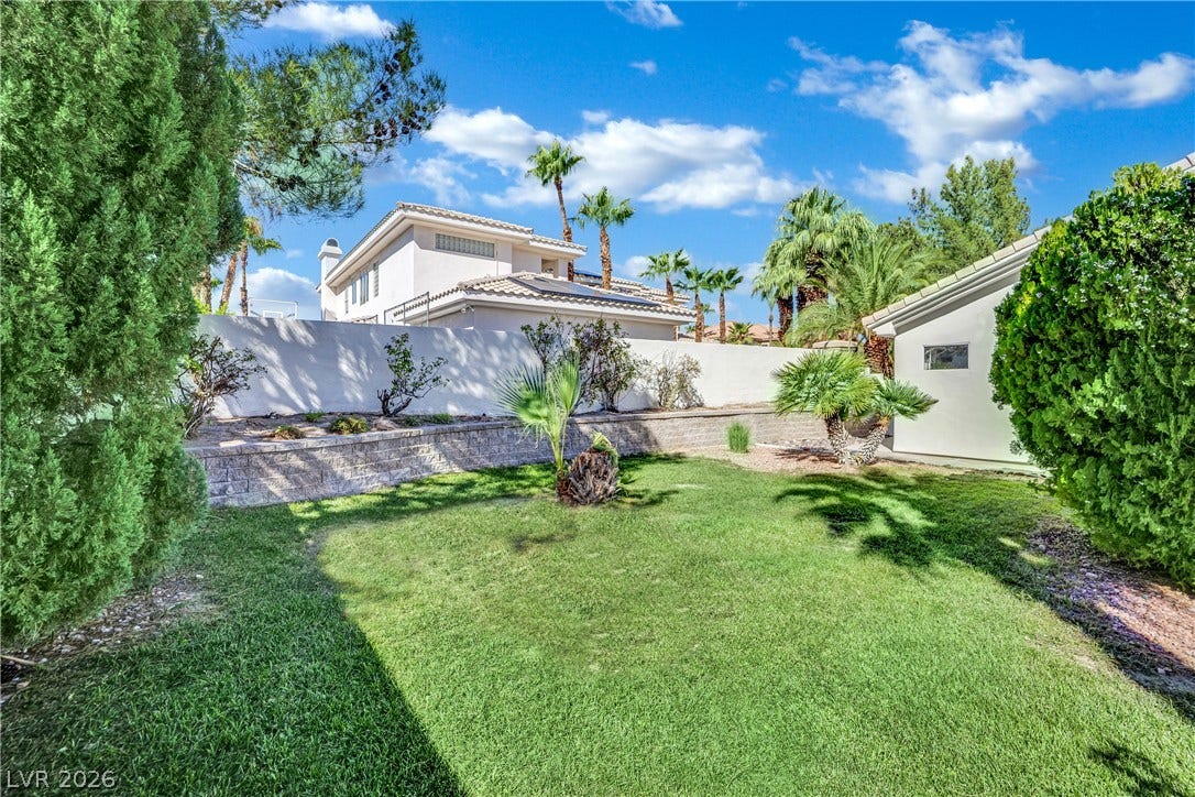 Mature trees and neat stone retaining walls frame a verdant lawn under clear desert skies.