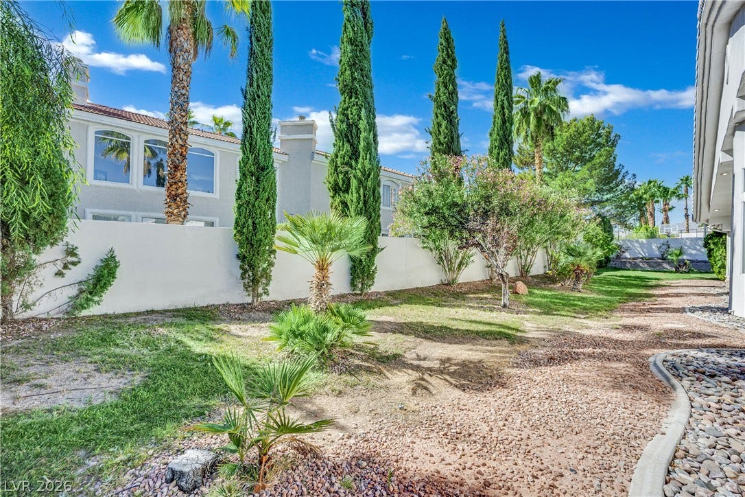 Towering cypress and palm trees line the enclosed yard with low-maintenance gravel landscaping.