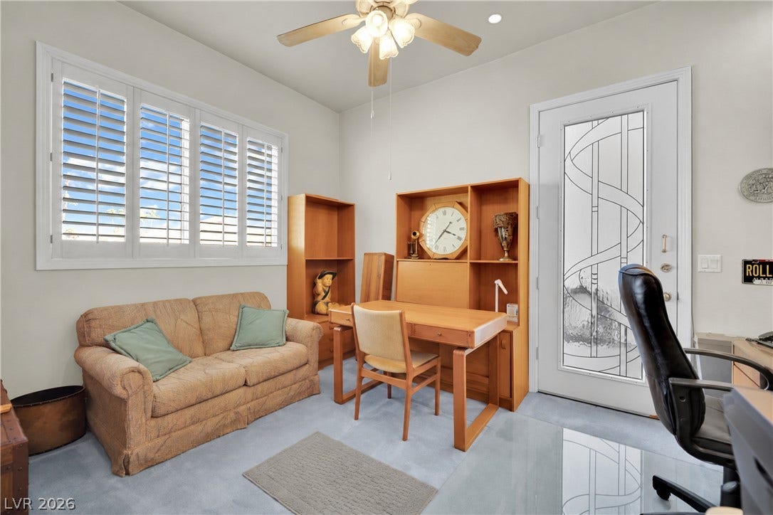 A versatile home workspace highlights glass-paneled entry door detail and plantation shutters.
