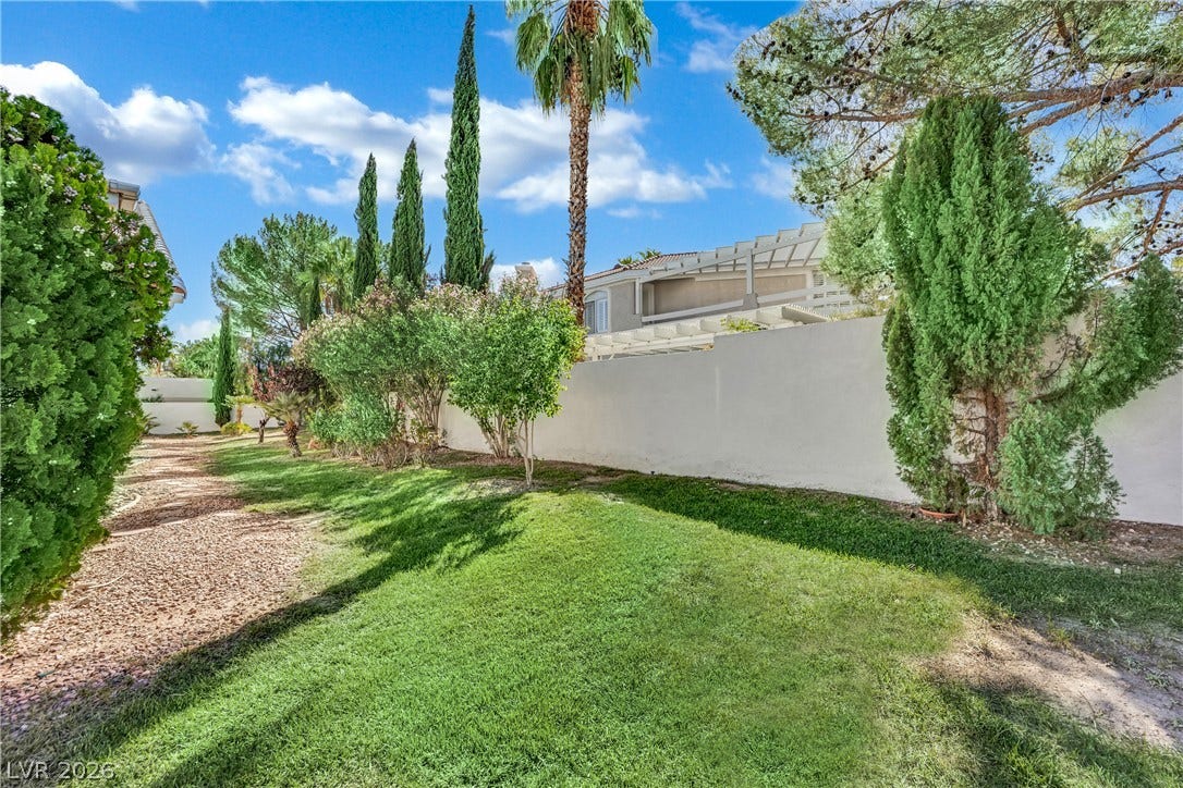 Mature trees and a solid privacy wall frame this grassy outdoor retreat.