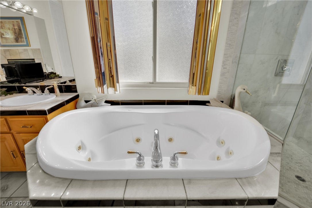A deep soaking tub sits beneath a large window in this tiled bathroom.