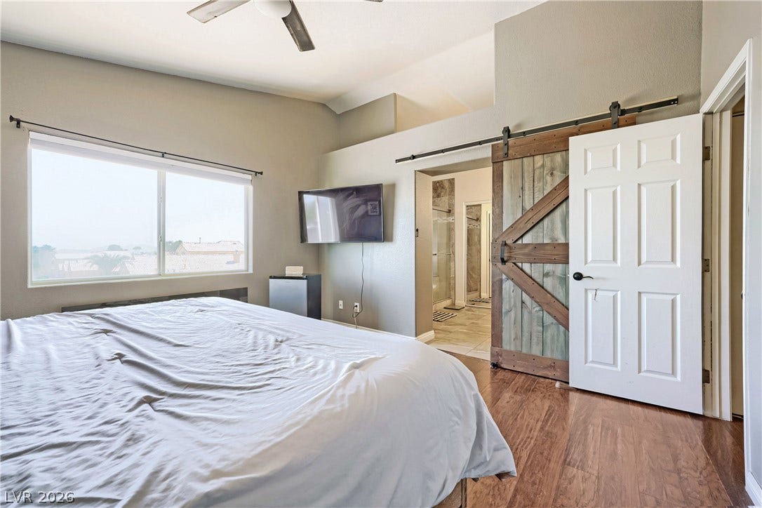 3536 Golden Pedal Street, Las Vegas, NV 89129 Rich wood flooring and a rustic sliding barn door enhance this airy primary suite.