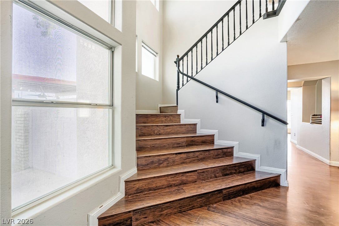 3536 Golden Pedal Street, Las Vegas, NV 89129 A striking wooden staircase ascends alongside tall windows, creating an airy and welcoming entrance.