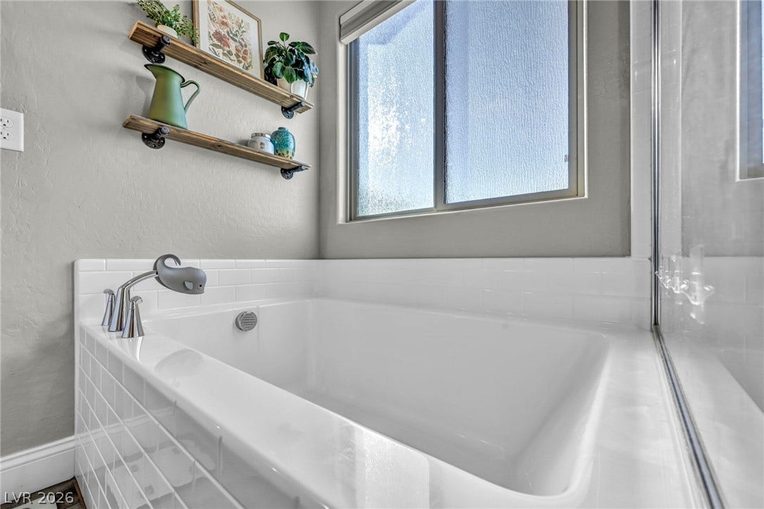 A deep soaking tub sits beneath a bright window framed by clean subway tile.