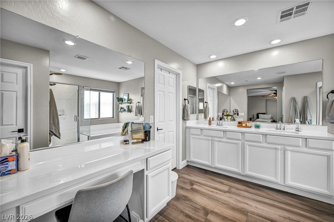 Recessed lighting illuminates this master bathroom with dual vanities and wood-look flooring.