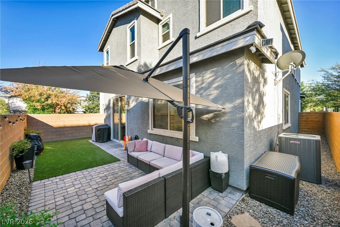 A paved patio space leads to a low-maintenance lawn enclosed by privacy fencing.