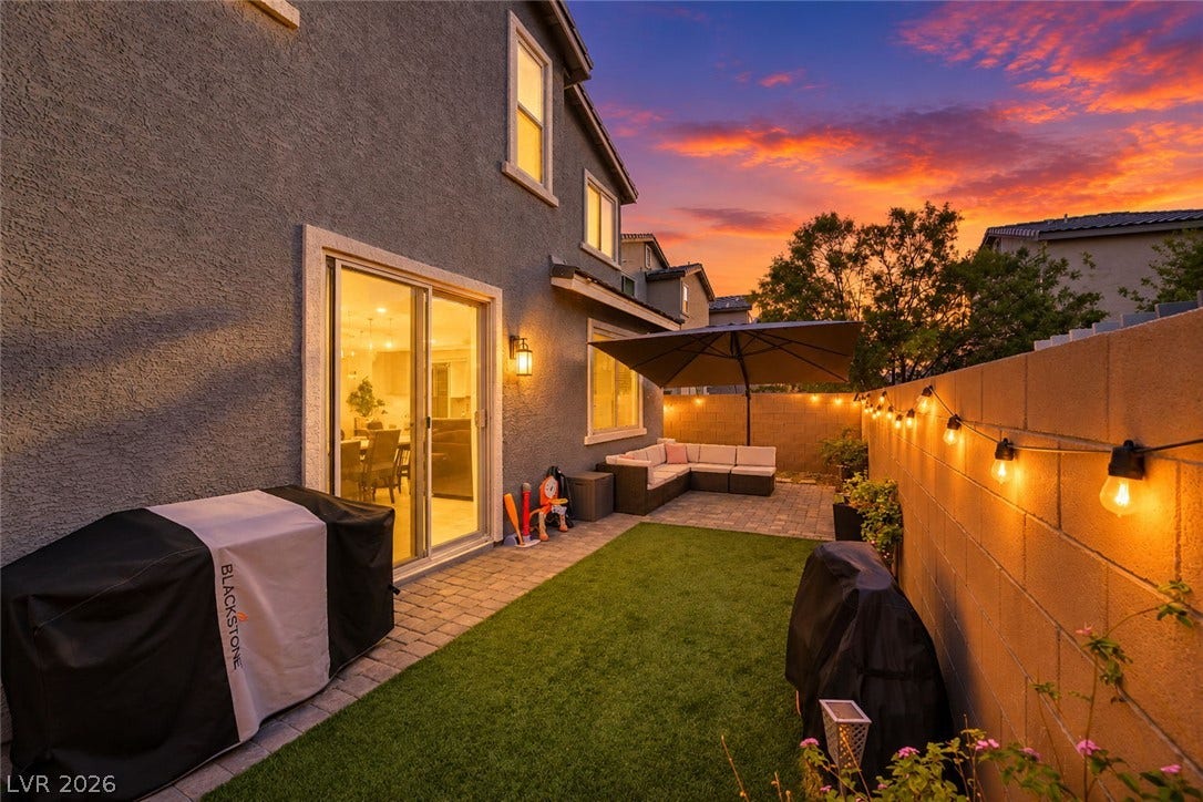 An inviting backyard patio features stone pavers, manicured turf, and stucco walls under evening skies.