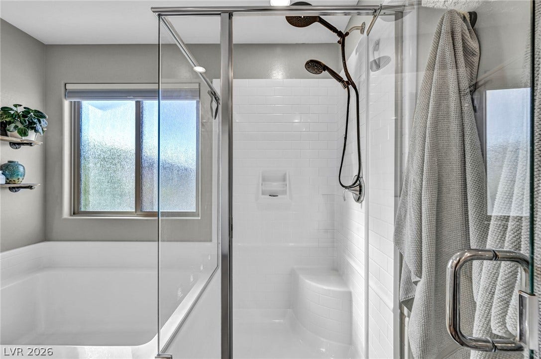 A glass-enclosed walk-in shower stands adjacent to a deep soaking tub beneath a frosted window.