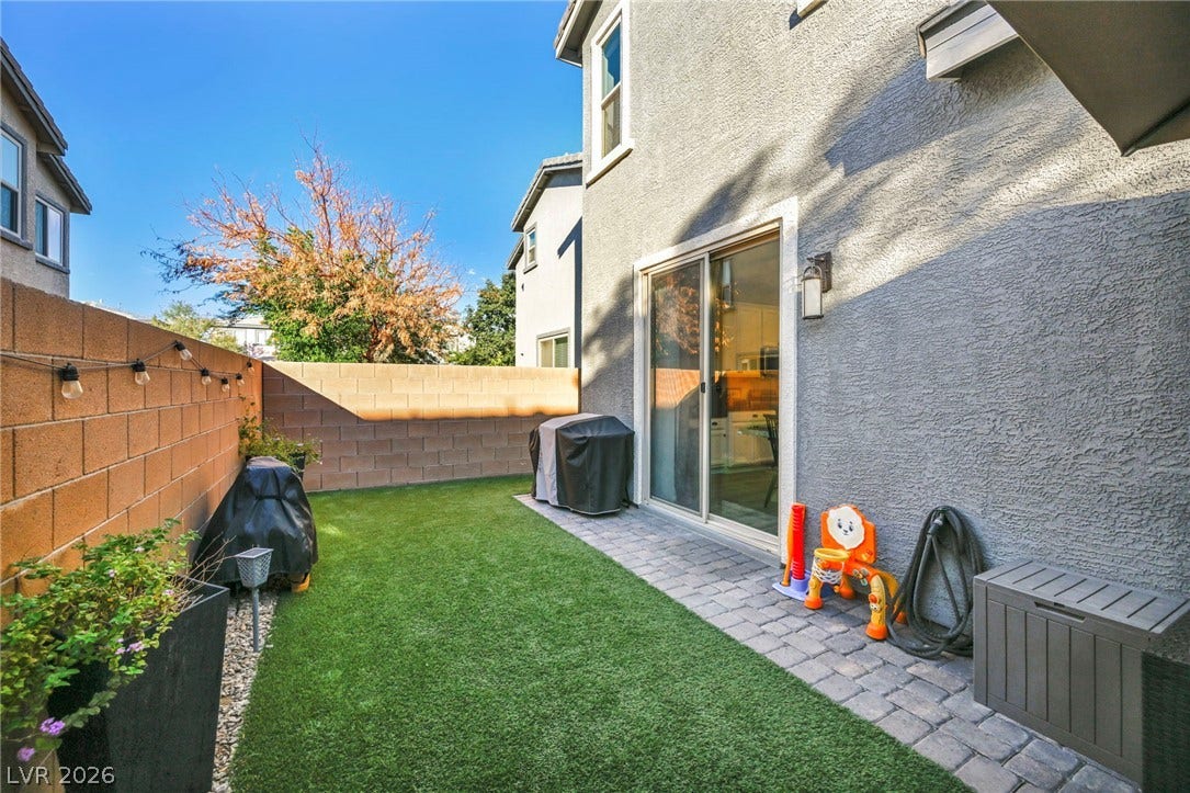 An enclosed backyard features a stone paver patio alongside a neat lawn area.