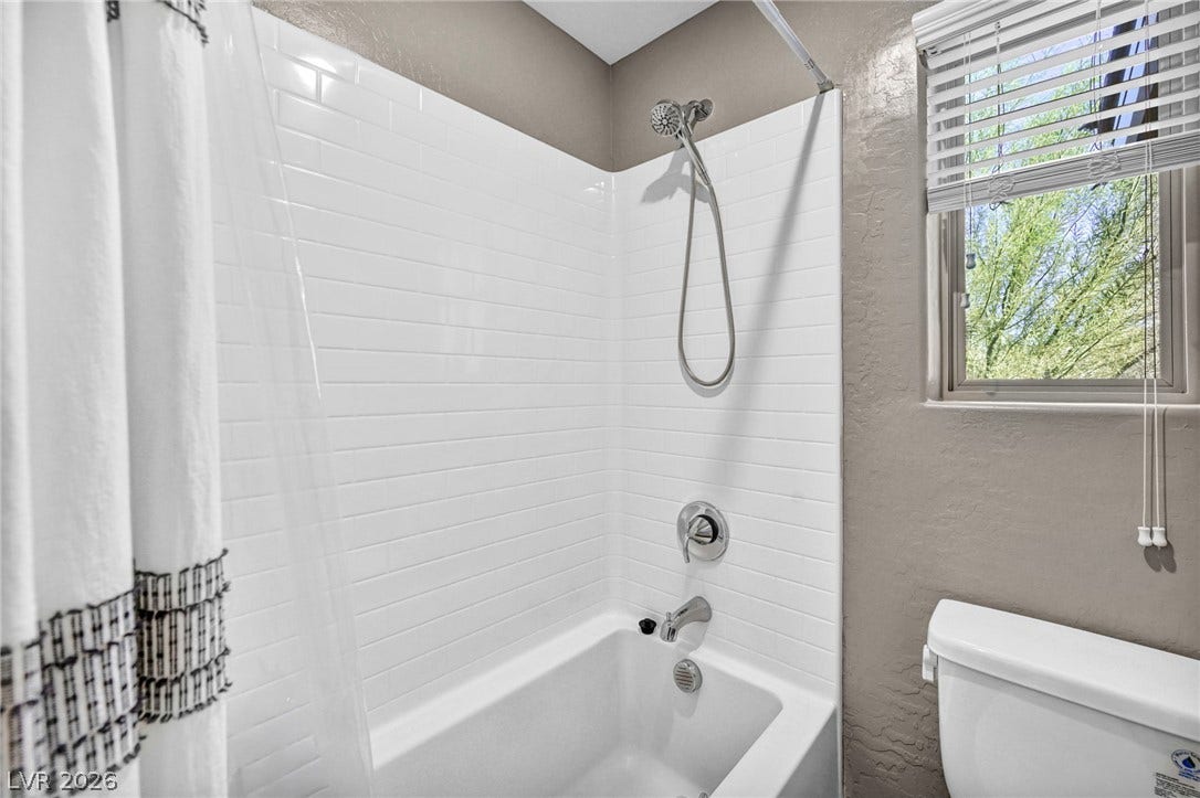 Crisp subway tile surrounds this classic shower and tub combination alongside a bright window.