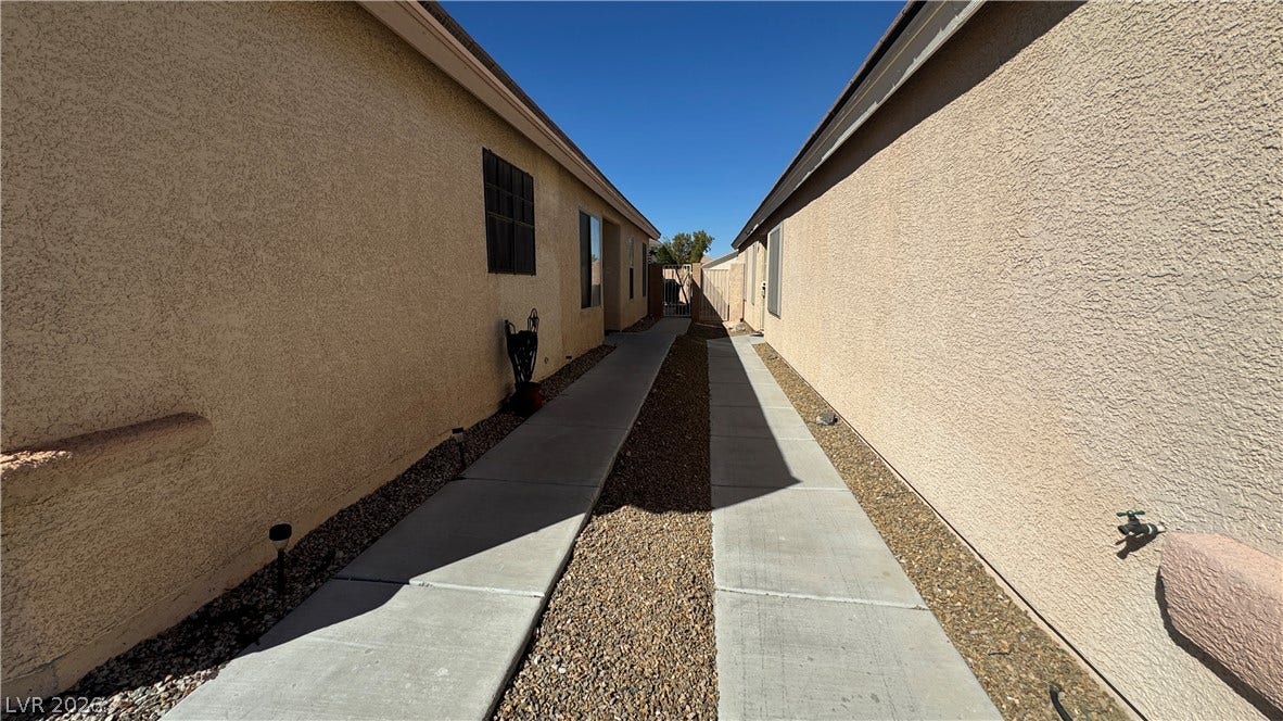 A clean concrete walkway extends along the stucco exterior under a clear blue sky.