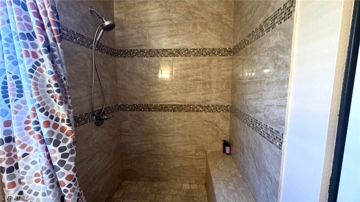 Glistening tilework surrounds a spacious walk-in shower featuring a built-in bench.