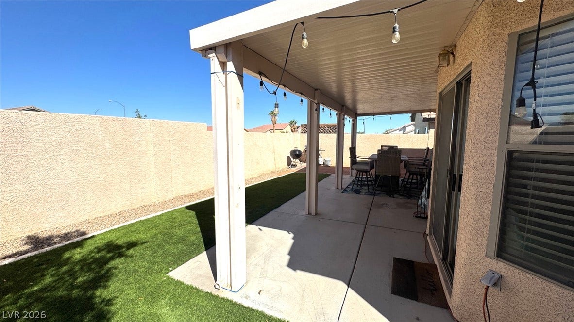 An inviting covered concrete patio overlooks the manicured green lawn and private yard.