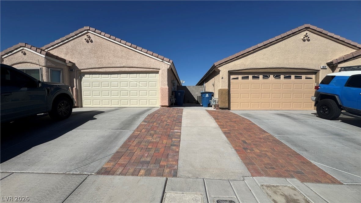 Matching stucco exteriors flanked by concrete and paver driveways under clear blue desert skies.